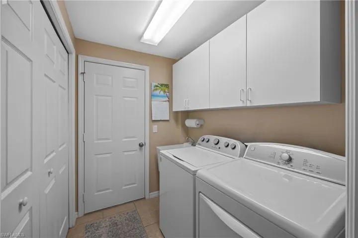 Laundry area with cabinets, washing machine and clothes dryer, and light tile patterned floors