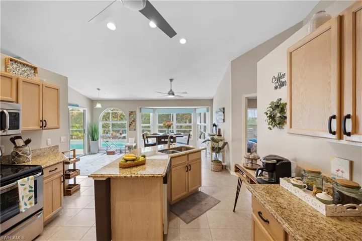 Kitchen featuring a center island with sink, stainless steel appliances, light brown cabinetry, light stone counters, and sink