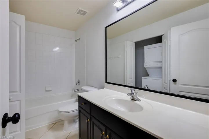 Full bathroom with vanity, stacked washer and clothes dryer, bathtub / shower combination, and light tile patterned flooring