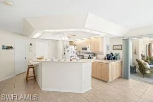 Kitchen featuring light countertops, white appliances, light tile patterned floors, light brown cabinetry, and a kitchen island