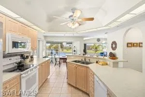 Kitchen featuring light tile patterned flooring, light countertops, white appliances, a tray ceiling, and light brown cabinetry