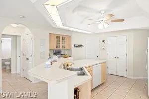 Kitchen with light countertops, a raised ceiling, arched walkways, a sink, and light tile patterned floors