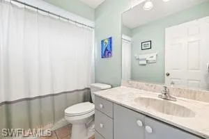 Full bath with curtained shower, toilet, tile patterned flooring, and vanity