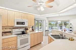 Kitchen with white appliances, a raised ceiling, light brown cabinets, a sink, and light tile patterned floors