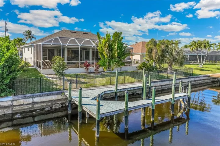 Dock featuring glass enclosure, a water view, a sunroom, a fenced backyard, and a patio