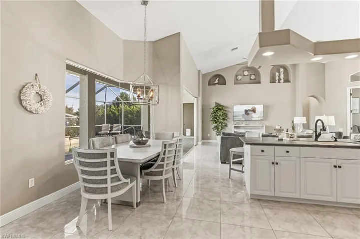 Dining space with high vaulted ceiling, light marble finish flooring, a chandelier, and a sunroom