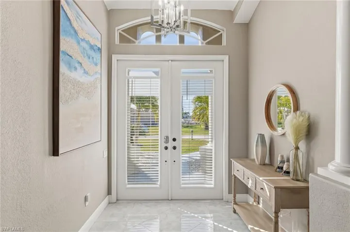 Doorway to outside featuring french doors, a chandelier, marble finish flooring, and a textured wall