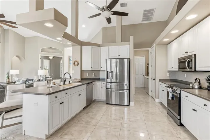 Kitchen with stainless steel appliances, high vaulted ceiling, dark countertops, ceiling fan, and a peninsula