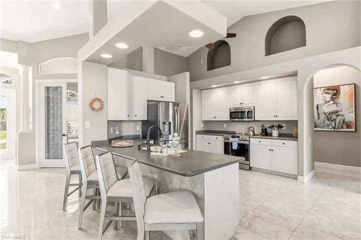 Kitchen with arched walkways, dark countertops, a peninsula, stainless steel appliances, and white cabinetry