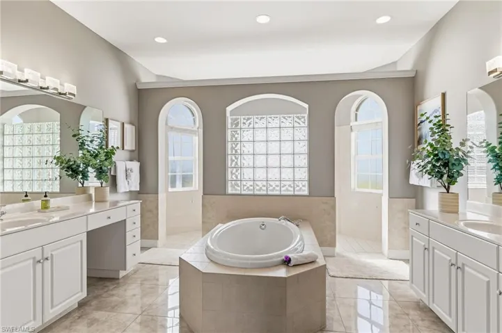 Full bathroom featuring two vanities, a walk in shower, a bath, and wainscoting