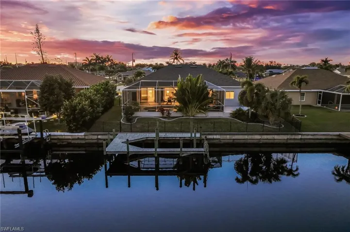 Back of house at dusk featuring boat lift, glass enclosure, and a water view