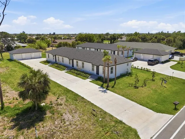 Modern multi-unit property featuring white exterior siding, dark shingle roofing, multiple driveway access points, and mature palm trees