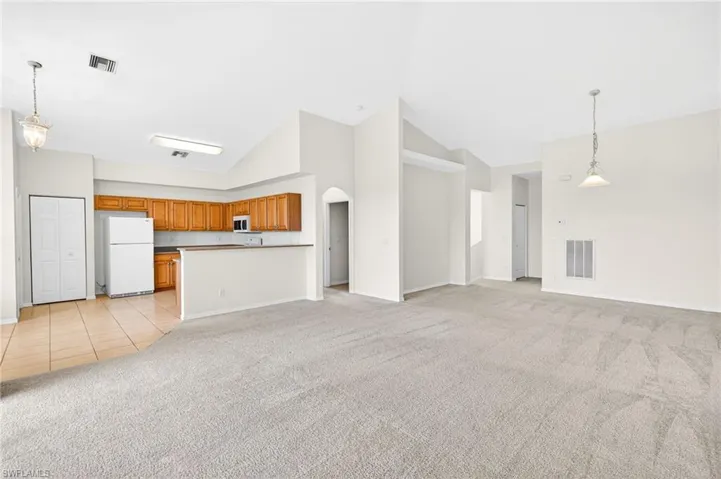 Unfurnished living room with light colored carpet, arched walkways, high vaulted ceiling, and light tile patterned floors