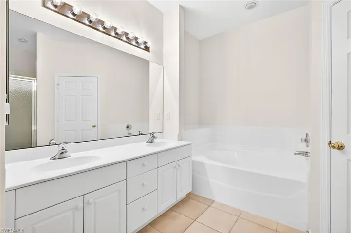 Bathroom featuring double vanity, a shower stall, a garden tub, and light tile patterned flooring