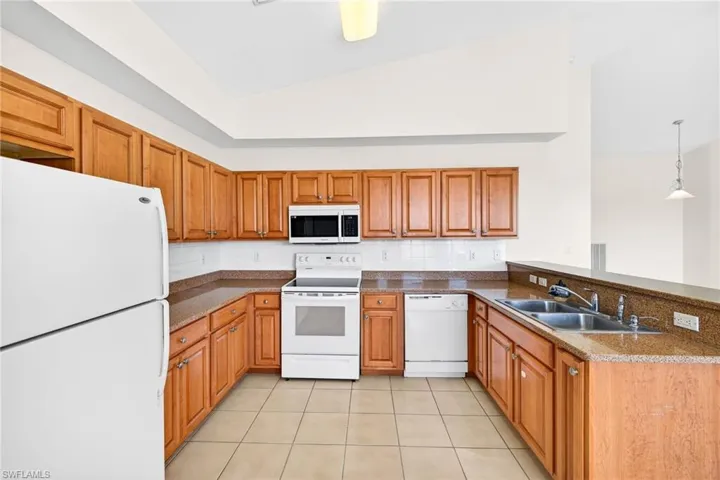 Kitchen featuring white appliances, brown cabinets, a peninsula, hanging light fixtures, and backsplash