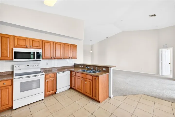 Kitchen featuring light carpet, white appliances, open floor plan, lofted ceiling, and brown cabinets