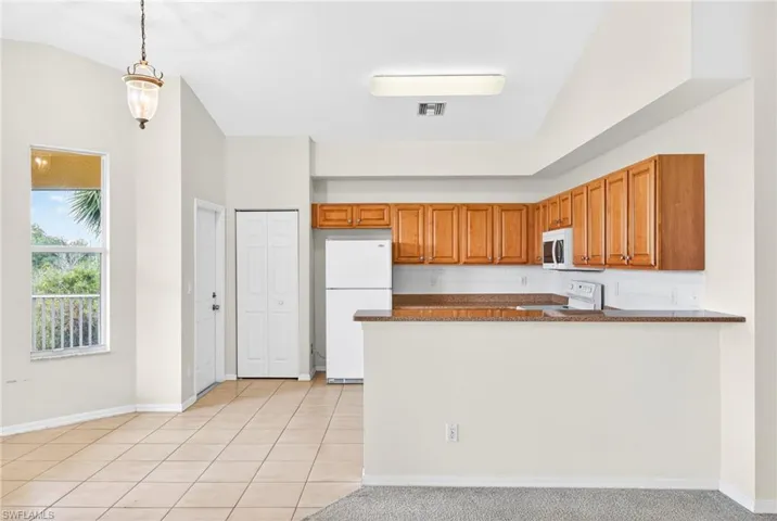 Kitchen featuring brown cabinets, pendant lighting, white appliances, dark stone countertops, and backsplash