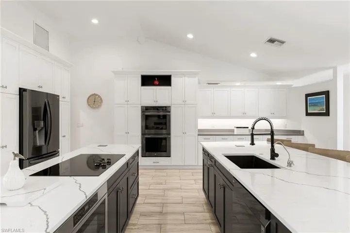 Kitchen with white cabinetry, stainless steel appliances, lofted ceiling, and sink