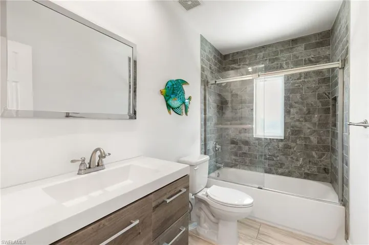 Full bathroom with tile patterned floors, vanity, shower / bath combination with glass door, and toilet