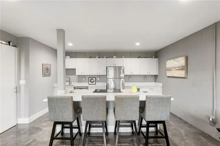 Kitchen with concrete floors, a breakfast bar area, stainless steel refrigerator, white cabinets, and an island with sink
