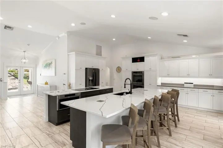 Kitchen featuring a center island with sink, fridge with ice dispenser, stainless steel double oven, a kitchen breakfast bar, and sink