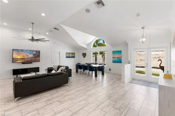 Living room featuring lofted ceiling, ceiling fan with notable chandelier, and light tile patterned floors