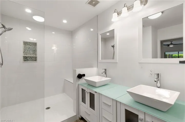 Bathroom with double vanity, ceiling fan, and a tile shower