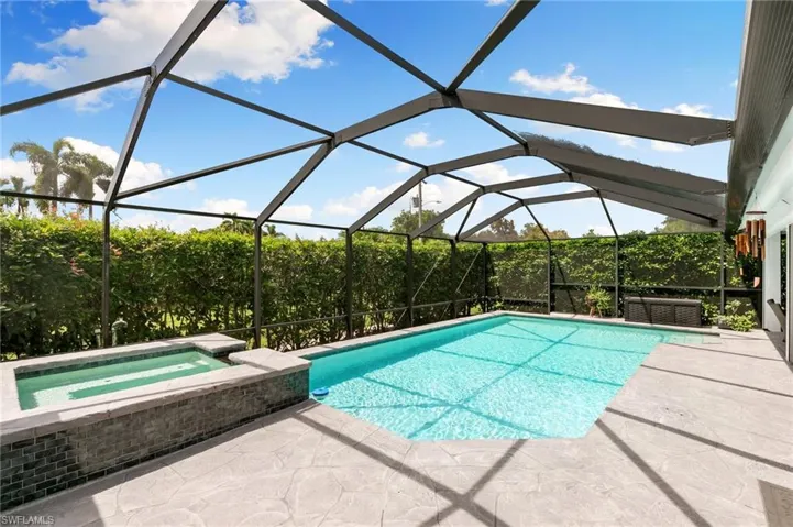 View of pool with an in ground hot tub, glass enclosure, and a patio area