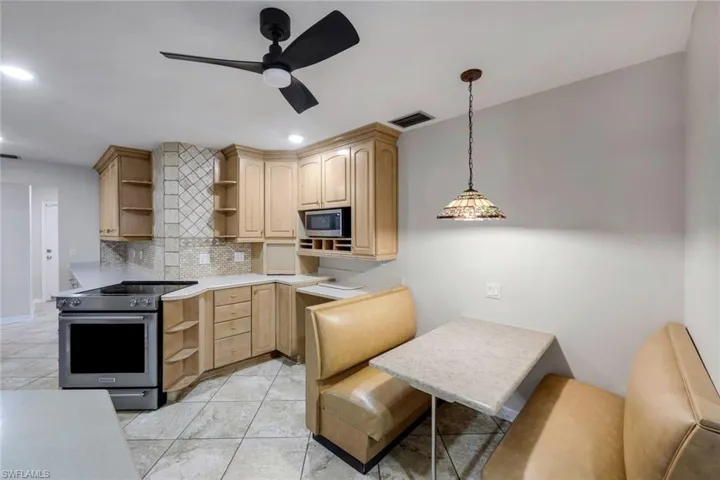 Kitchen featuring light wood cabinetry with built-in microwave, stainless steel range, light-toned countertops, and a tiled backsplash
