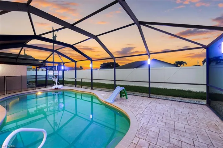 Screened-in pool area featuring a freeform swimming pool, decorative stamped concrete patio, and a privacy fence