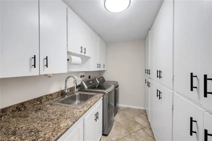 Laundry area featuring abundant white cabinetry with black hardware, a stainless steel sink with a high-arc faucet, and mottled countertop