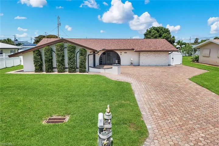 Single-story residence featuring a paver driveway, manicured front lawn, and a white fence