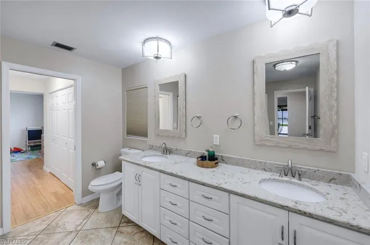 Dual vanity featuring white cabinetry with brushed nickel hardware, light-toned stone countertops, and undermount sinks