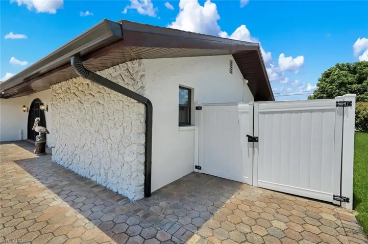 Exterior features include a textured stone wall, a white vinyl fence with gate, dark gutters, and a window with dark trim