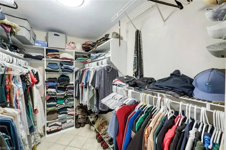 Walk-in closet featuring white wire shelving, built-in cubbies, hanging rods, and light-toned tile flooring