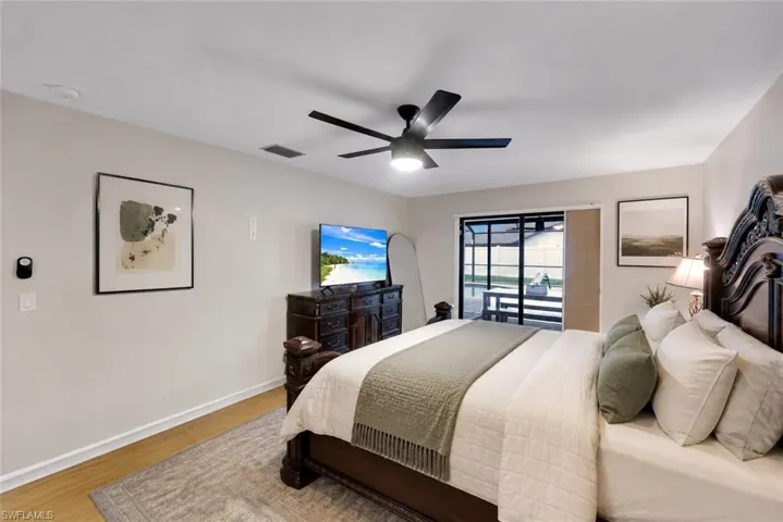 Bedroom with light wood-finish flooring, a contemporary ceiling fan with integrated lighting, and direct access to an outdoor area via sliding glass doors