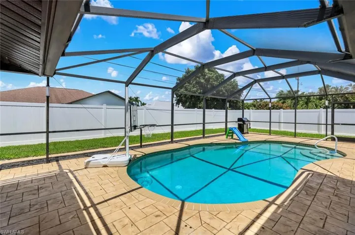 Screened outdoor pool area featuring a freeform pool with integrated steps, patterned concrete paver decking, and a white vinyl privacy fence