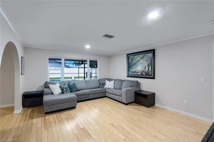 Open-concept living area featuring wood-finish flooring, white baseboards, crown molding, and recessed lighting