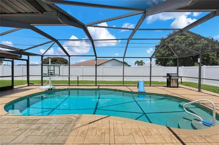 Screened-in pool area featuring a freeform pool, textured concrete deck, and perimeter fencing