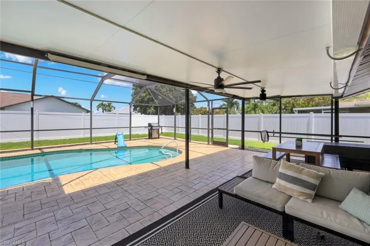 Screened outdoor living area featuring a rectangular pool, paver patio, white privacy fence, and covered lanai with ceiling fans