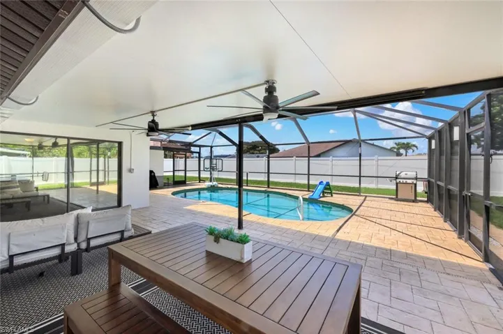 Screened-in outdoor living space featuring a covered patio, ceiling fans, a swimming pool, and paver decking