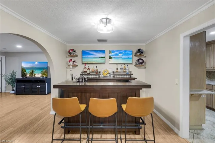 Custom built-in bar with a dark wood-finish countertop and base, illuminated by a semi-flush mount ceiling light