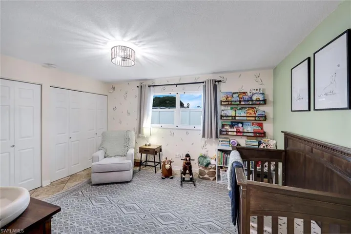 Room featuring a single window with curtains, a dark wood-finish crib, two bi-fold closet doors, a decorative ceiling light fixture, and tile flooring