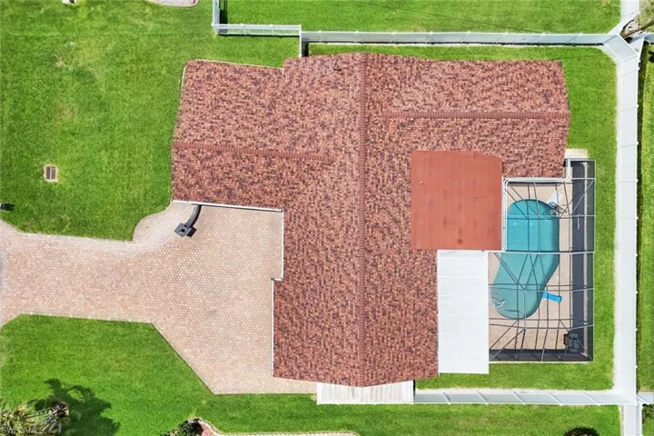 Expansive property featuring a textured roof, screened pool enclosure, paved driveway, and manicured lawns