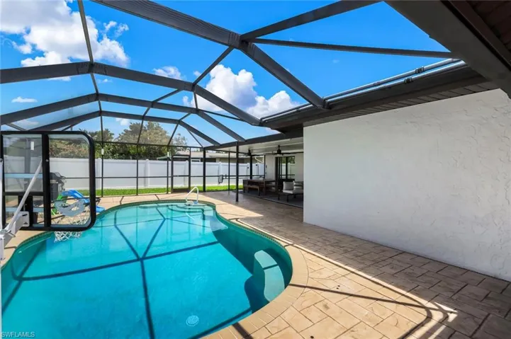 Screened pool enclosure featuring a freeform swimming pool with steps, a white privacy fence, an exterior wall with stucco finish, and stamped concrete decking