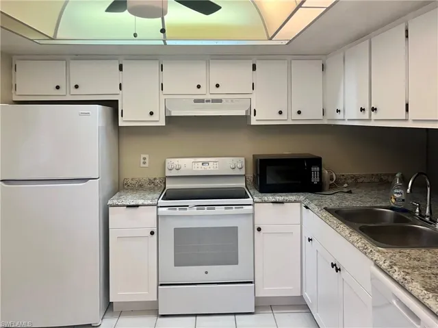 Kitchen with light tile patterned flooring, ceiling fan, white cabinets, white appliances, and sink