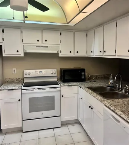 Kitchen featuring white appliances, light tile patterned floors, white cabinets, ceiling fan, and sink