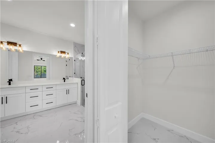Bathroom featuring a sink, a spacious closet, marble finish floor, baseboards, and double vanity