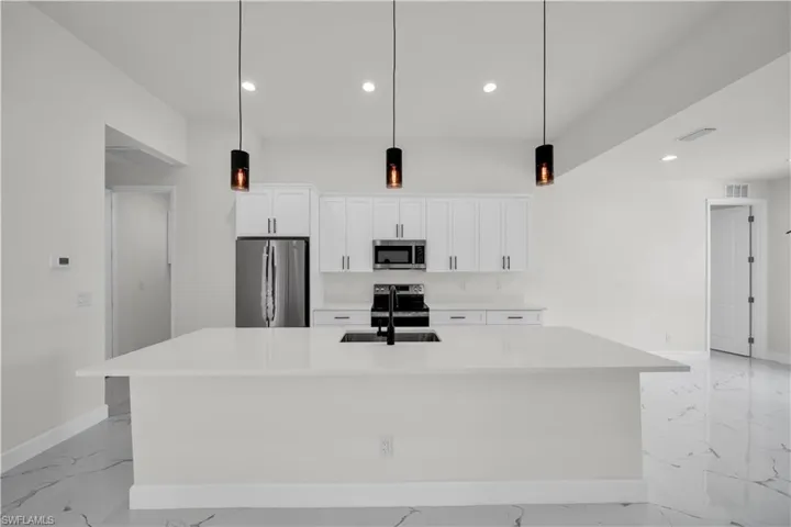 Kitchen featuring white cabinetry, stainless steel appliances, a spacious island, marble finish floor, and a sink