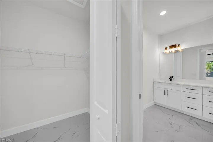 Full bath with baseboards, marble finish floor, a walk in closet, and vanity